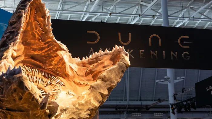 A Sandworm from Dune Awakening, in front of a sign for the game.