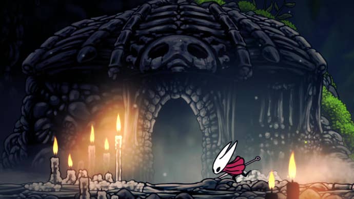 Hornet, the main character of Hollow Knight: Silksong, enters a foreboding-looking building lit outside by candles.